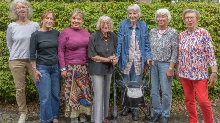 Sieben ältere Frauen stehen gemeinsam im Freien, lächeln und posieren für ein Gruppenfoto.