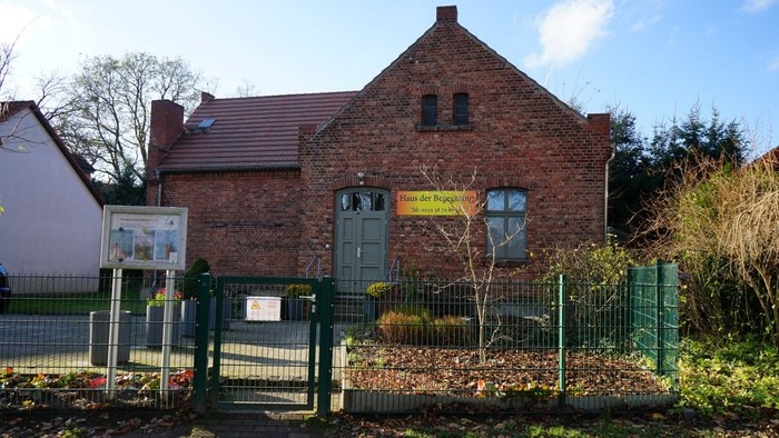 Backsteingebäude mit Schild 'Haus der Begegnung', davor Zaun und Vorgarten.