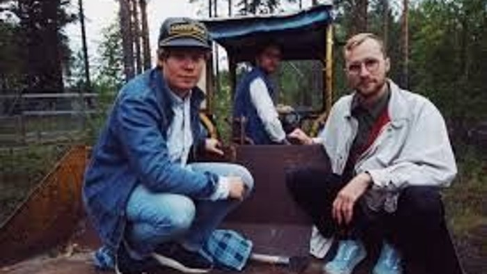 To personer sidder på en træbænk i et skovområde og poser sammen udendørs.