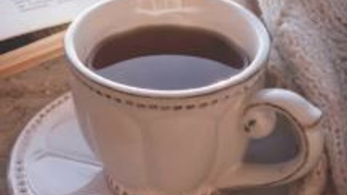 Eine dampfende Tasse Kaffee steht auf einer verzierten Untertasse neben einem gemütlichen Gebäckstück auf einer rustikalen Oberfläche.