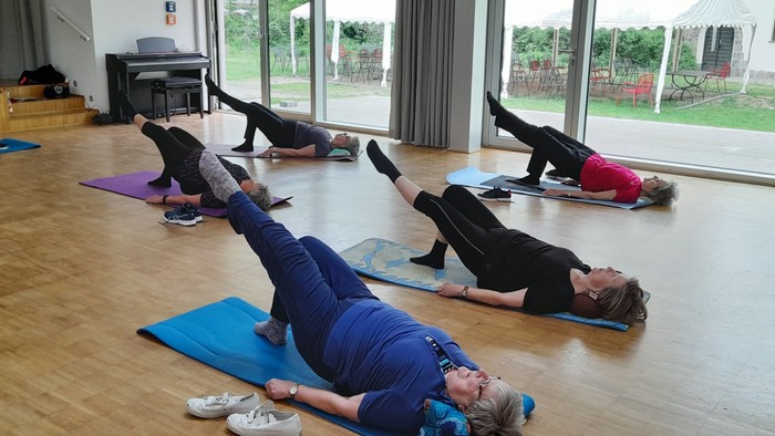 Eine Gruppe von Menschen übt Yoga in einem Raum mit großen Fenstern.