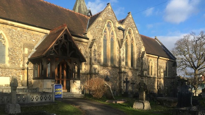 Church with tall spire and arched windows, surrounded by gravestones and trees.