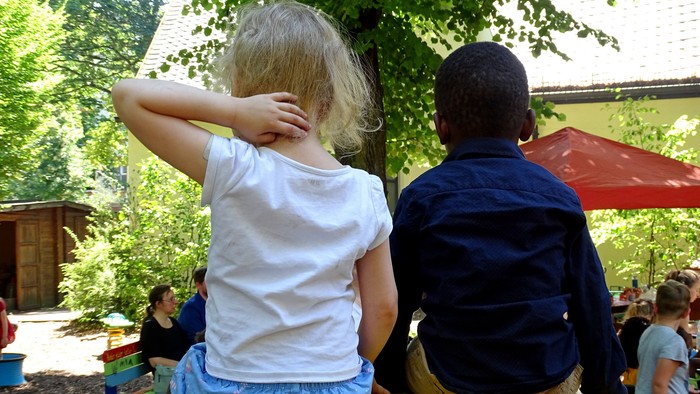 Zwei Kinder sitzen auf einer bunten Bank im Garten.