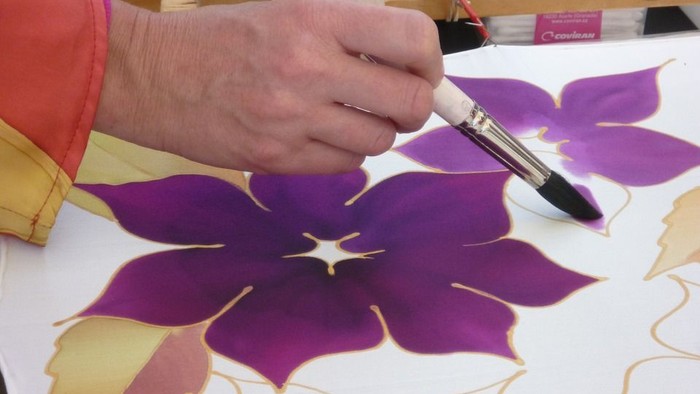 Hand malt mit Pinsel eine lila Blume auf weißem Stoff