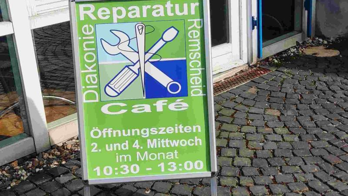 Ein grünes Schild wirbt für ein Reparatur-Café, das am 2. und 4. Mittwoch jedes Monats von 10:30 bis 13:00 Uhr geöffnet ist.