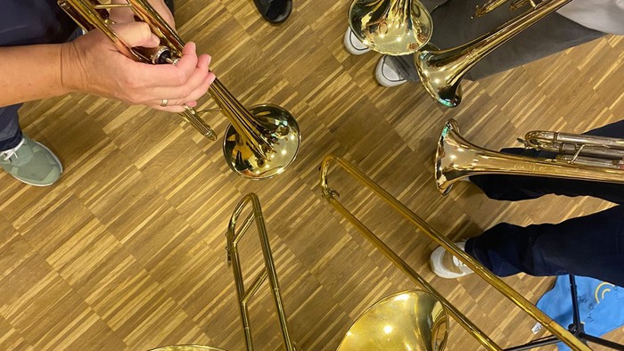 Eine Gruppe von Blechblasinstrumenten, darunter Trompeten und Posaunen, auf einem Holzboden ausgelegt.