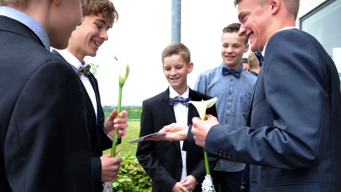 En gruppe unge mænd i formelle klæder holder blomster og laver selie.