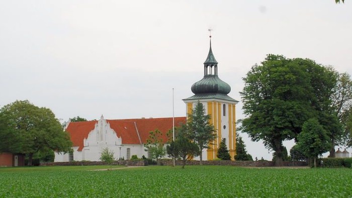 En grøn og åben mark med et gult tårn og røde huse.