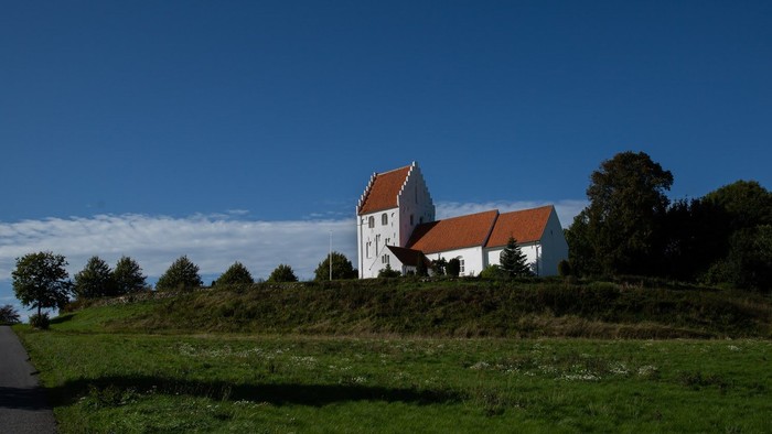 En lille kirke med røde tag på en bakke ved en vej