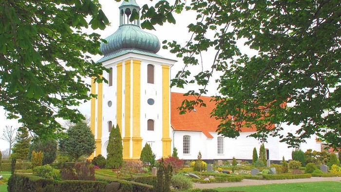 Et gult og hvidt kloster med grøn kuppel og omgivet af en have med træer og buske