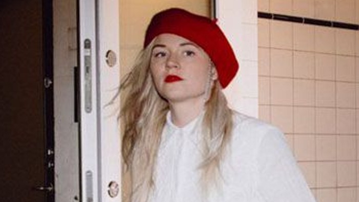 En person i en hvid top, sorte bukser og en rød hat bærer blomster, mens vedkommende går udenfor om natten.