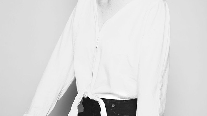 En afbalanceret kvinde i en hvid bluse og sorte bukser sidder selvsikkert på en skammel.