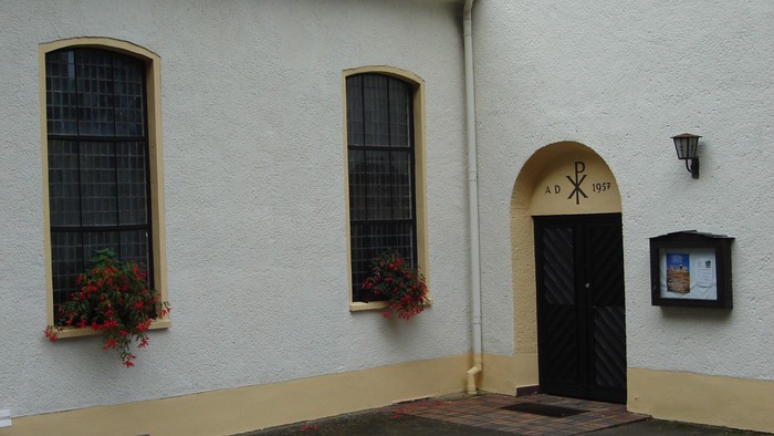 Weißes Gebäude mit zwei Fenstern und einer Tür, die mit Blumenkästen geschmückt sind