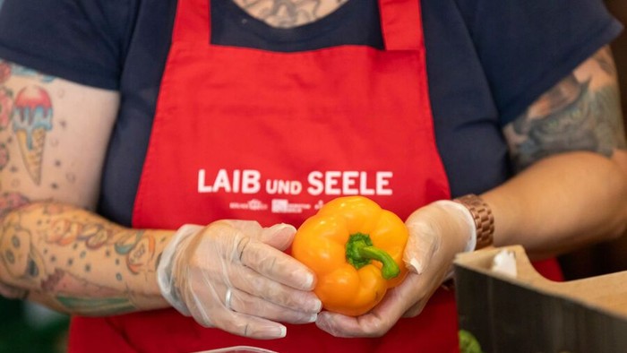 Person hält eine gelbe Paprika, trägt eine rote Schürze und Handschuhe.