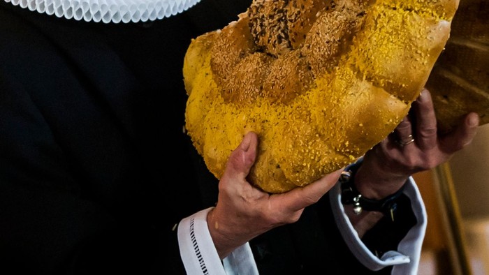 En person holder et stort, gyldenbrunt brød med en smuldrende top.