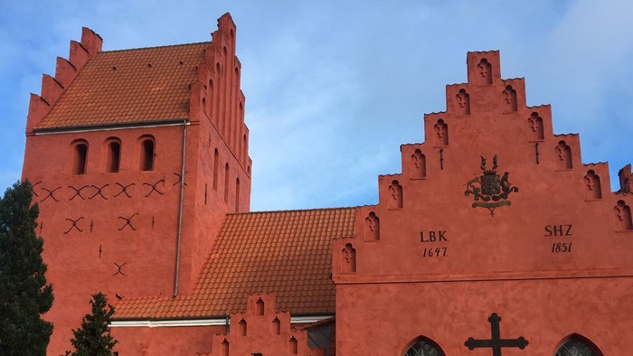 Røde kirke med tårn og gravsteder i forgrunden