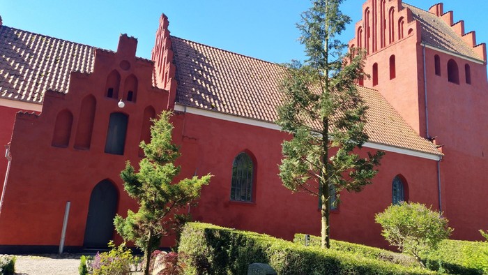 Rødt kirkebygning med spisse tårn og grønne træer foran