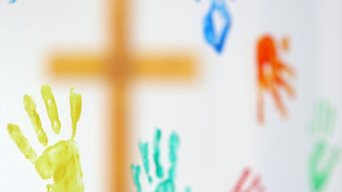 Bunte Kinderhandabdrücke und ein Kreuz auf hellem Hintergrund, die Einheit und Kreativität symbolisieren.