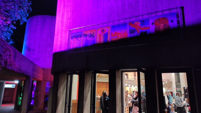 Moderner Gebäudeeingang, beleuchtet mit lebendigem violettem Licht, der Menschen zeigt, die einen Veranstaltungsraum betreten.