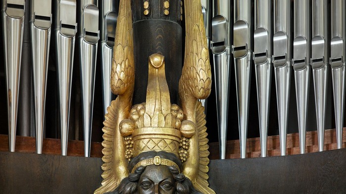 Das Bild zeigt eine verzierte Holzskulptur vor einem Orgelpfeifenhintergrund