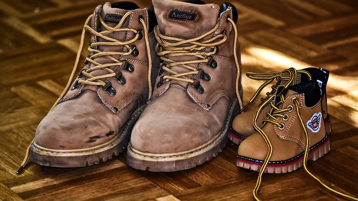 Ein Paar braune Arbeitsstiefel und ein kleineres Paar Stiefel auf einem Holzboden.