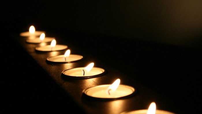 Seven lit candles in a row against a dark background.