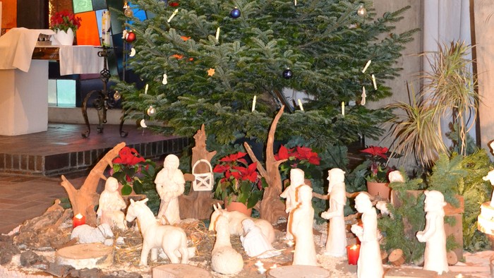 Weihnachtsbaum mit Krippenszene vor einem Buntglasfenster
