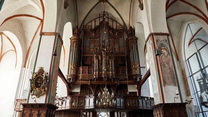 Historische große Pfeifenorgel in einem prunkvollen, gewölbten Kircheninnenraum mit hölzernen Kirchenbänken und dekorativen Wandmalereien.
