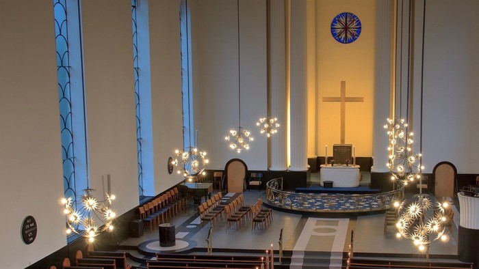 Indre del af kirke med lysdekorerede træer og alter med kors