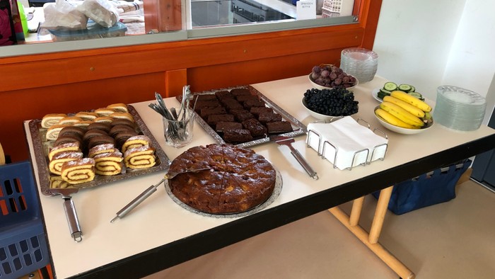 Auf dem Tisch stehen verschiedene Kuchen und Süßigkeiten, darunter Schokoladenkuchen, Donuts und Bananen.
