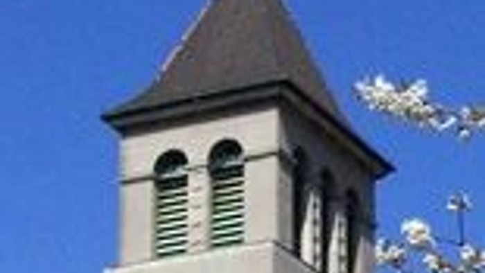 Ein hoher Turm mit Uhr und spitzem Dach vor blauem Himmel.