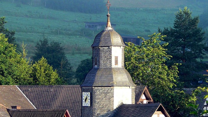Dorfkirche mit grünem Hügel im Hintergrund
