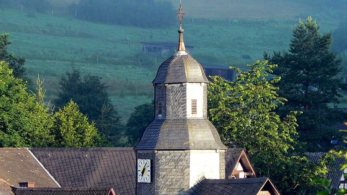 Dorfkirche mit grünem Hügel im Hintergrund