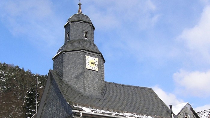 Graues Kirchgebäude mit Uhrturm und Schnee auf dem Dach