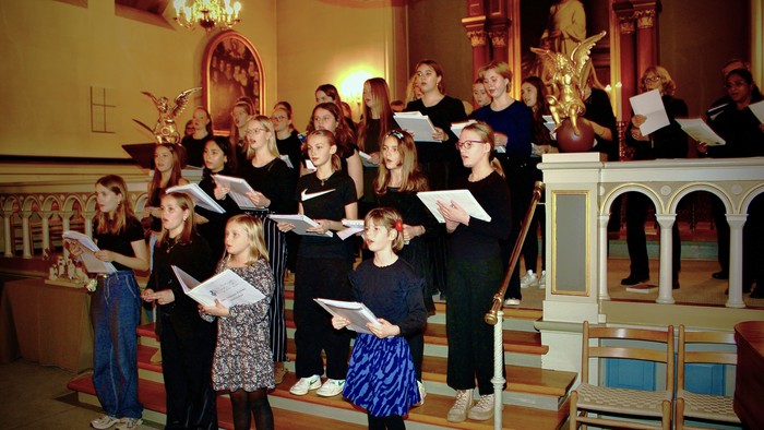 En kirkekor med børn og voksne, der synger i koret