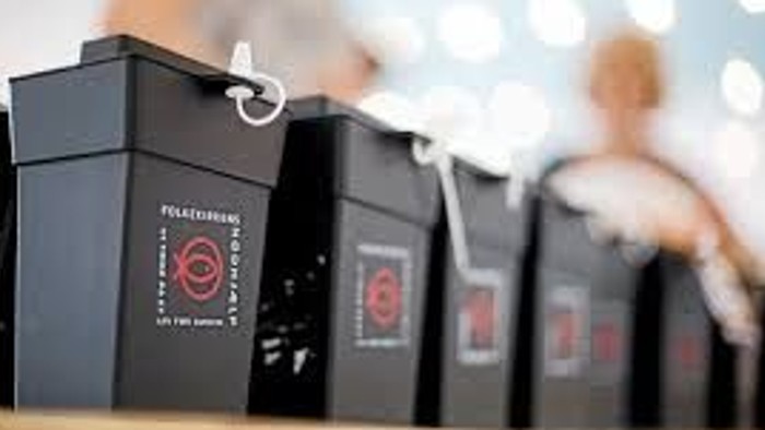 En række svarte vinflasker med røde etiketter og hængeslør.