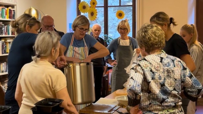 Eine Gruppe von Menschen nimmt an einem Kochkurs teil, sie stehen um einen Tisch mit Kochutensilien und einem großen Topf.