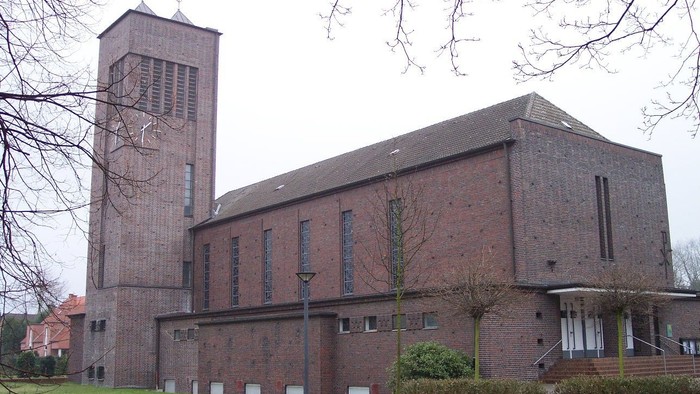 Moderne Backsteinkirche mit hohem Glockenturm in einer gestalteten, offenen Grünanlage.
