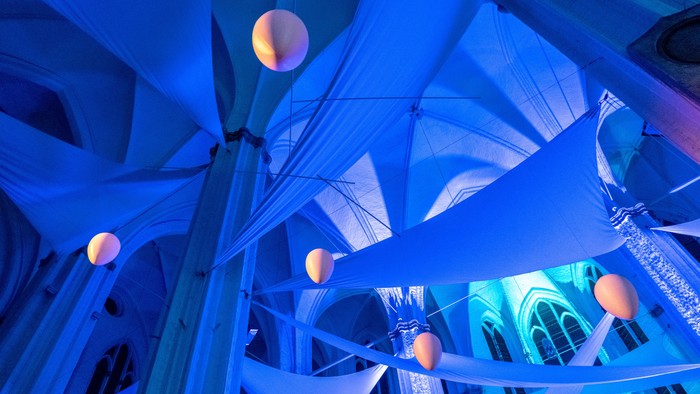 Moderne architektonische Innenraumgestaltung mit beleuchteten blauen Bändern und leuchtenden kugelförmigen Lichtern vor einer dramatischen Decke.