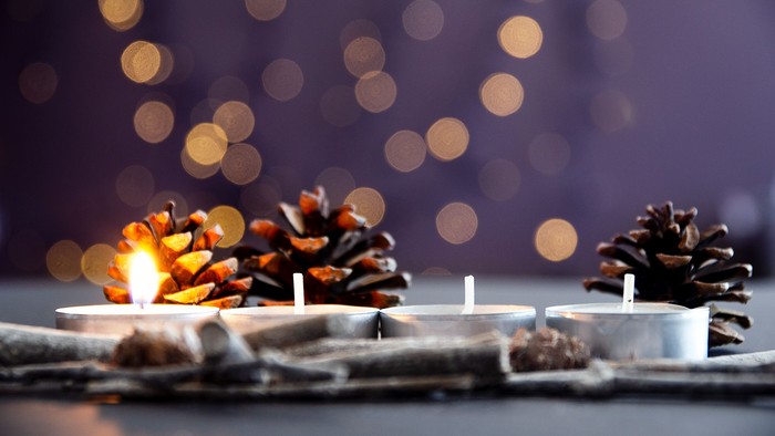 Das Bild zeigt Adventsdekoration mit 4 Teelichtern, wovon eins brennt.