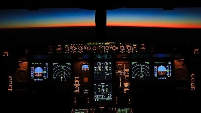 Luftaufnahme des Cockpits mit Fluginstrumenten und Steuerungselementen vor einem atemberaubenden Sonnenuntergangshorizont.