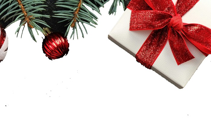 Weihnachtsbaum, geschmückt mit festlichem Schmuck, Christbaumkugeln und einem verpackten Geschenk mit roter Schleife.