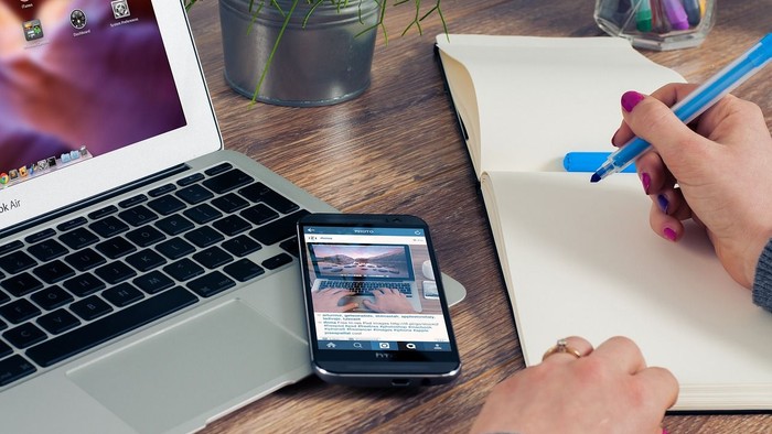 Eine Person arbeitet an einem Schreibtisch mit Laptop, Smartphone und Notizbuch.