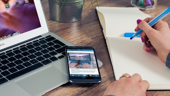 Eine Person arbeitet an einem Schreibtisch mit Laptop, Smartphone und Notizbuch.