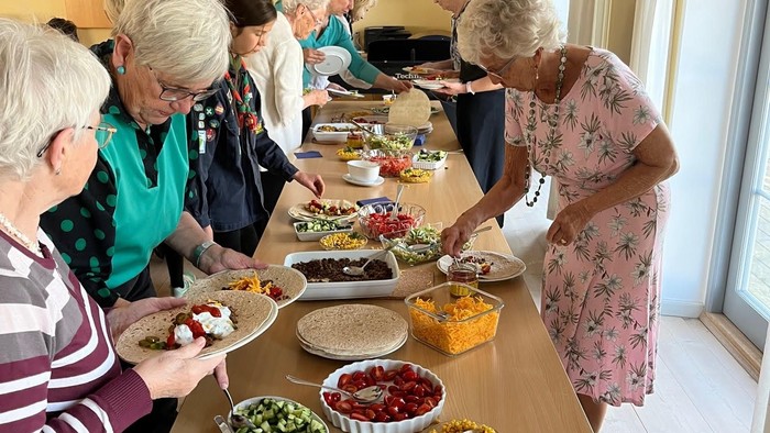 Gruppe af mennesker, der forsyner sig selv fra et buffetbord med forskellige retter og snacks.