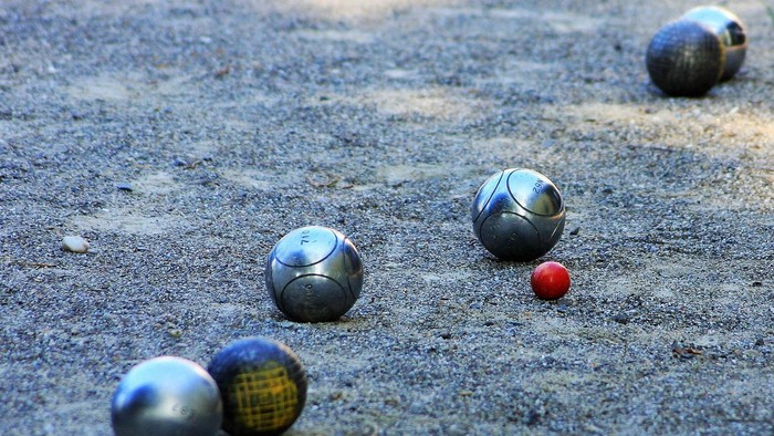 Auf einem sandigen Spielfeld angeordnete Pétanque-Kugeln mit einer roten Zielkugel in der Mitte.