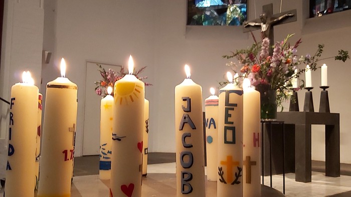 Kirchliche Kerzen mit Namen und Herzen, davor ein Blumenstrauß