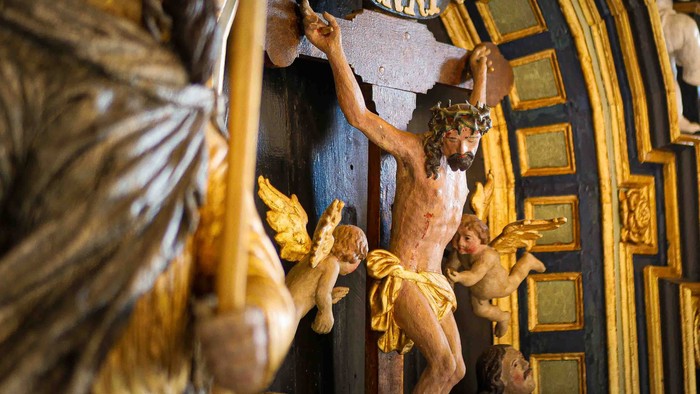 Indviklet religiøs skulptur, der forestiller Kristus på korset omgivet af kerubiske figurer i en prægtig indramning.