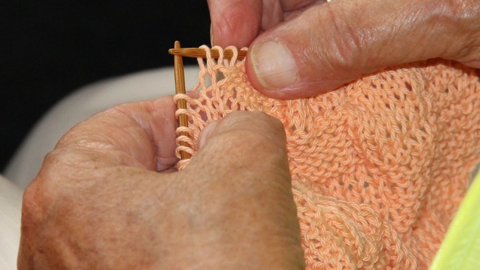 Hænder, der strikker på lys-orange strikketøj