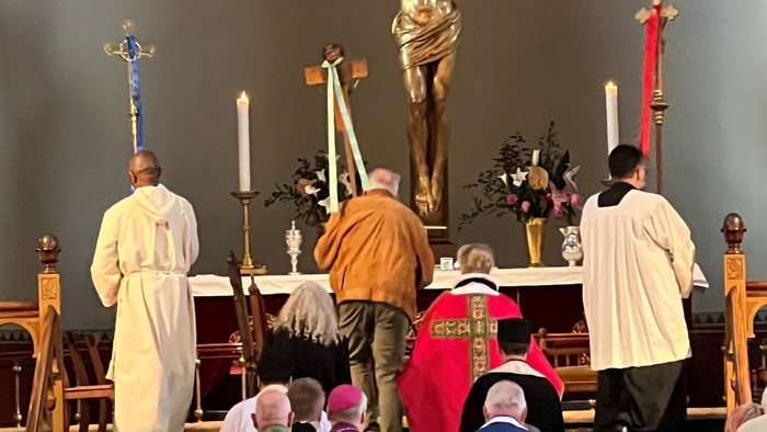 Religiøs ceremoni med gejstlige i liturgiske klæder omkring et krucifiks i en kirke.